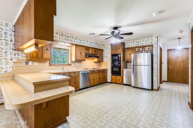 138 Cypress Dr, Opelousas, LA 70570 - kitchen featuring black appliances, under cabinet range hood, brown cabinets, light countertops, and wallpapered walls