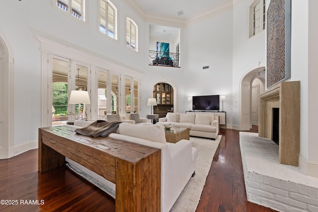 12425 N Marcus Rd, Abbeville, LA 70510 - living area featuring dark wood-type flooring, a towering ceiling, arched walkways, a brick fireplace, and baseboards
