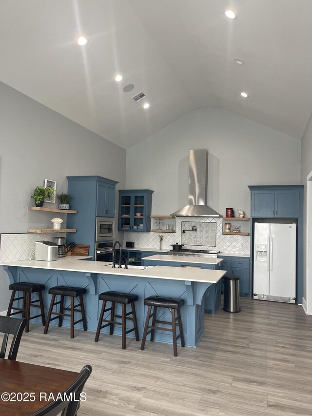 5087 Natali Rd, Lake Charles, LA 70607 - kitchen with open shelves, stainless steel appliances, wall chimney range hood, blue cabinetry, and high vaulted ceiling