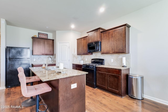 206 Agrarian Ave, Rayne, LA 70578 - kitchen featuring black appliances, a sink, light wood finished floors, an island with sink, and light stone counters