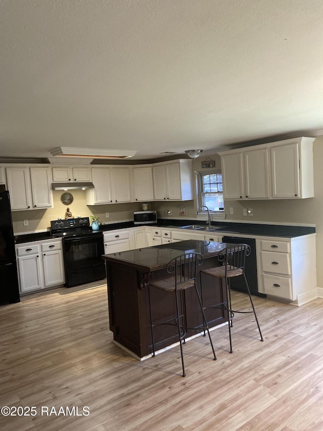 232 Mills St, Scott, LA 70583 - kitchen with black appliances, dark countertops, under cabinet range hood, light wood finished floors, and a textured ceiling