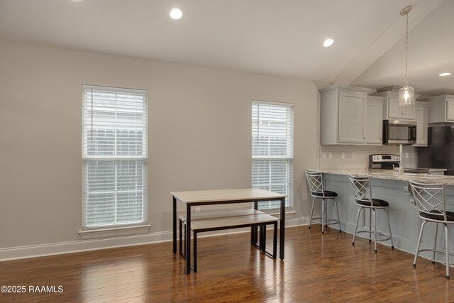 310 Harvest Ln, Abbeville, LA 70510 - kitchen with stainless steel microwave, stove, a kitchen bar, dark wood finished floors, and light stone counters