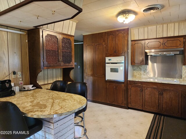 2115 Vige St, Opelousas, LA 70570 - kitchen with oven, under cabinet range hood, light floors, light countertops, and wood walls