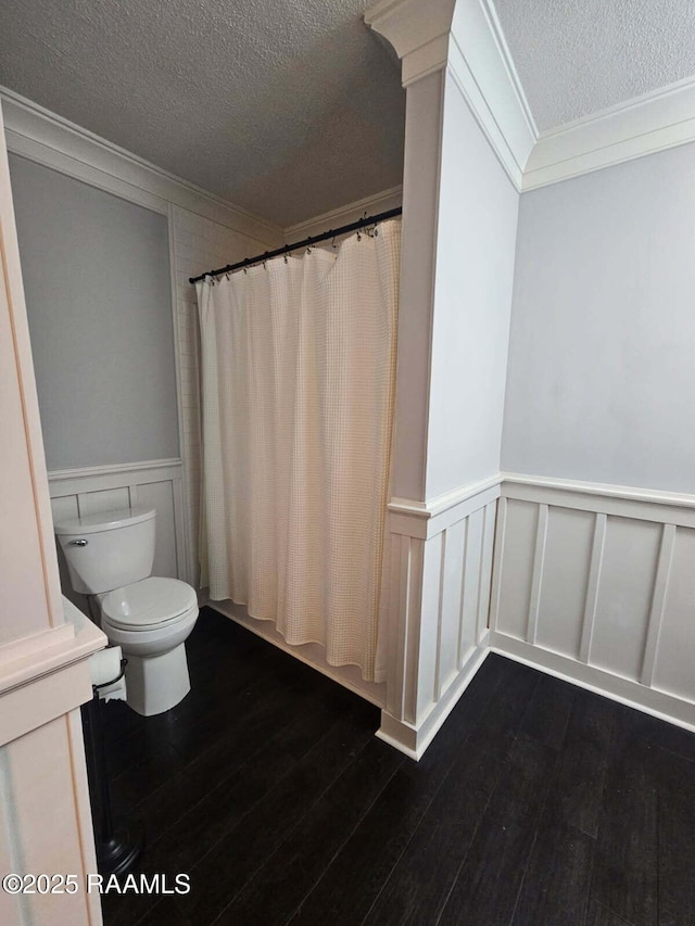 full bath featuring a textured ceiling, ornamental molding, wainscoting, wood finished floors, and curtained shower