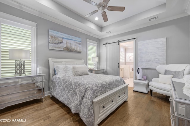 403 Catalina Ln, Youngsville, LA 70592 - bedroom featuring a barn door, a raised ceiling, wood finished floors, ensuite bath, and a ceiling fan