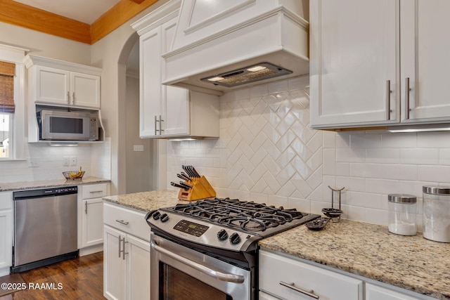 203 Whispering Meadows Rd, Broussard, LA 70518 - kitchen with stainless steel appliances, premium range hood, backsplash, white cabinets, and arched walkways