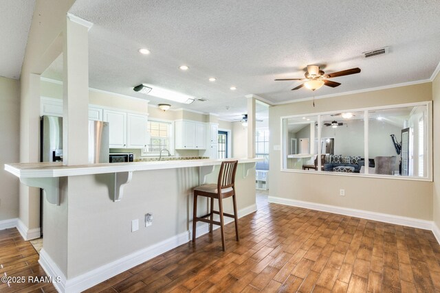 13723 Lynnedale Loop, Abbeville, LA 70510 - kitchen featuring a ceiling fan, a breakfast bar area, a textured ceiling, white cabinets, and wood finished floors