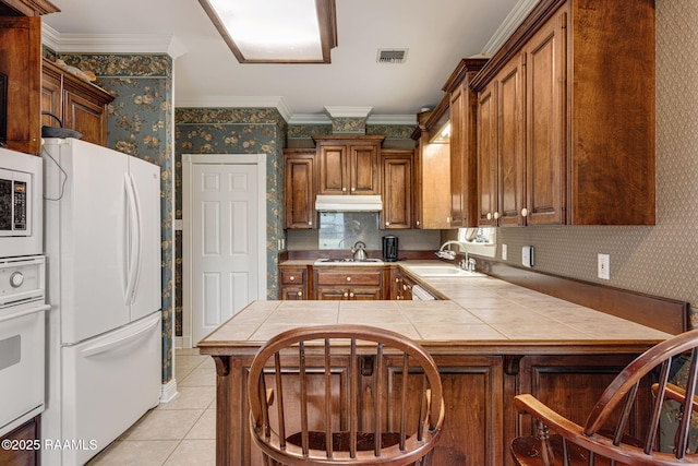 104 Briarfield Dr, Carencro, LA 70520 - kitchen featuring white appliances, wallpapered walls, tile counters, under cabinet range hood, and light tile patterned floors