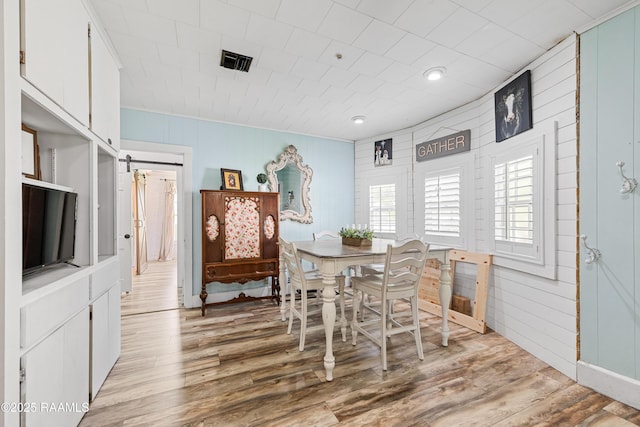 1054 Main St, Parks, LA 70582 - dining space featuring light wood-style floors, a barn door, crown molding, and wooden walls