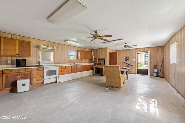 7011 Cameron St, Duson, LA 70529 - kitchen featuring white electric range, under cabinet range hood, wooden walls, brown cabinetry, and plenty of natural light