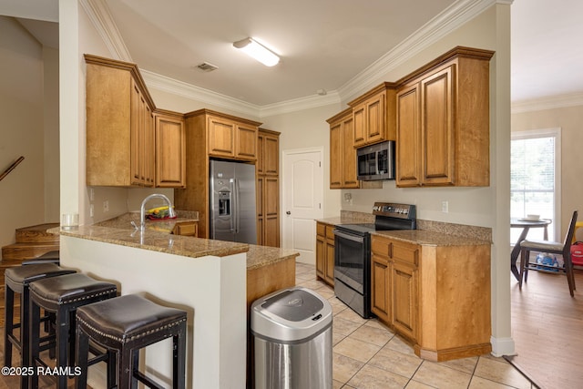 742 Hummingbird Ln, New Iberia, LA 70563 - kitchen featuring appliances with stainless steel finishes, a kitchen breakfast bar, a peninsula, light stone counters, and brown cabinets