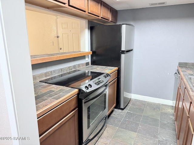 3121 Johnston St Unit 207, Lafayette, LA 70503 - kitchen featuring appliances with stainless steel finishes, tile countertops, brown cabinetry, and stone finish flooring