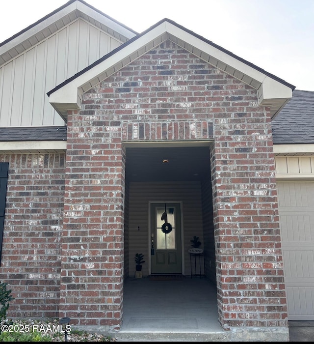 205 Acadian Lake Dr, Duson, LA 70529 - view of exterior entry featuring brick siding, a garage, board and batten siding, and a shingled roof