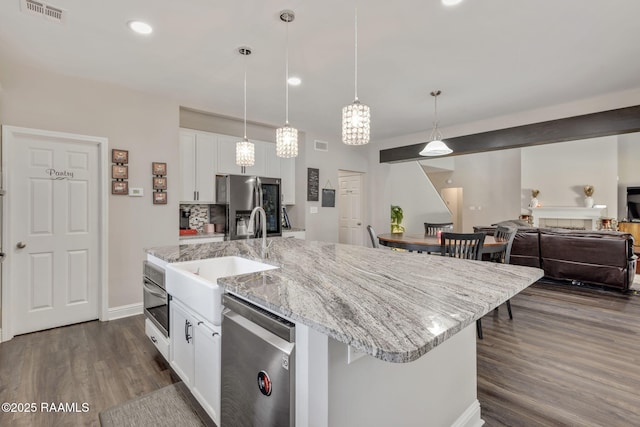 213 E Peck Blvd, Lafayette, LA 70508 - kitchen with stainless steel appliances, dark wood-style floors, white cabinetry, a center island with sink, and decorative light fixtures
