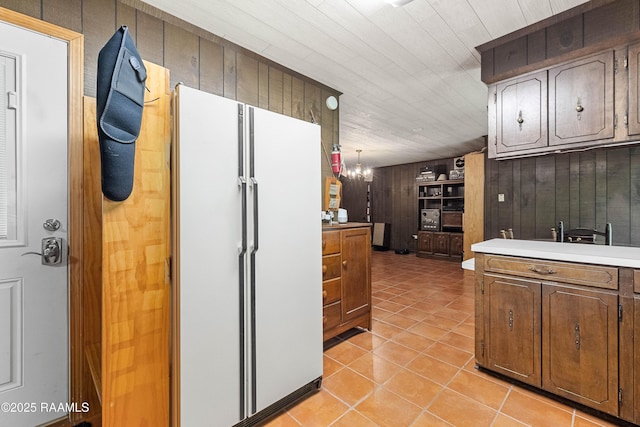 1912 Mimosa St, Abbeville, LA 70510 - kitchen featuring freestanding refrigerator, light tile patterned floors, light countertops, wooden walls, and a chandelier