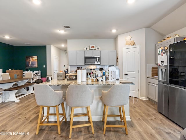 107 Southern Oak Dr, Lafayette, LA 70507 - kitchen featuring appliances with stainless steel finishes, a kitchen breakfast bar, light stone countertops, light wood finished floors, and recessed lighting