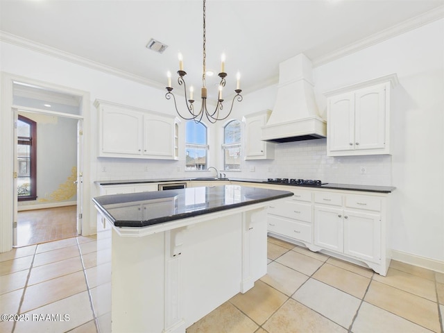 101 Lockeport Cir, Lafayette, LA 70508 - kitchen with custom range hood, crown molding, black cooktop, light tile patterned floors, and white cabinetry