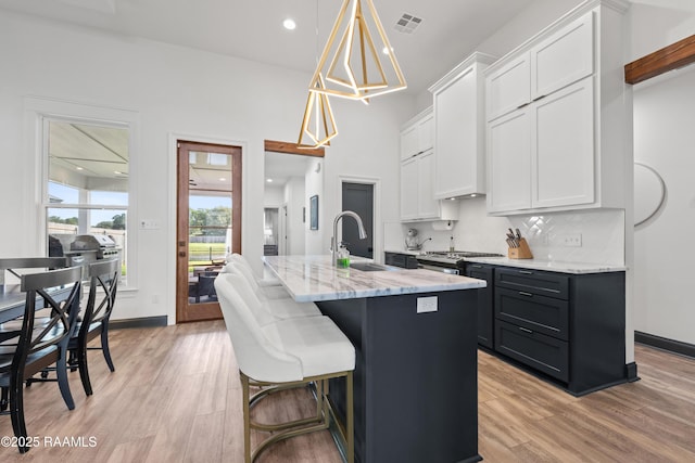 127 Lakes Edge Dr, Broussard, LA 70518 - kitchen featuring light stone countertops, white cabinets, light wood-type flooring, and a kitchen island with sink