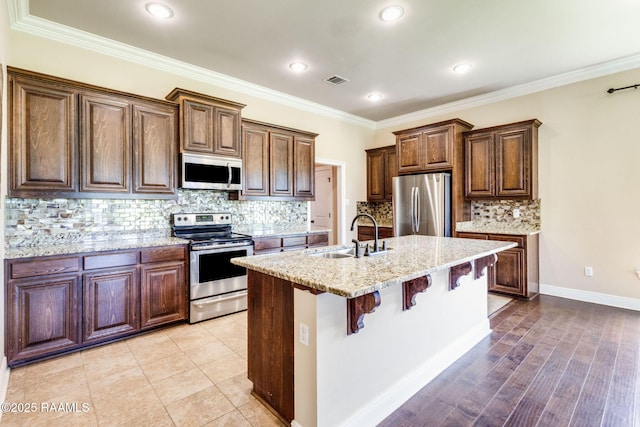 213 Hidden Ridge Dr, Lafayette, LA 70507 - kitchen featuring appliances with stainless steel finishes, a kitchen island with sink, light stone counters, tasteful backsplash, and a breakfast bar area