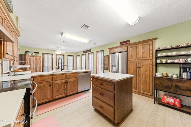 3317 Walnut Dr, Opelousas, LA 70570 - kitchen featuring stainless steel appliances, brown cabinetry, a kitchen island, a textured ceiling, and a peninsula