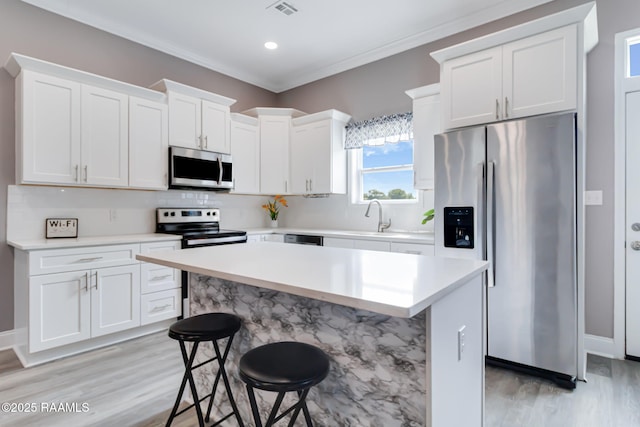 202 Saint Matthias Dr, Carencro, LA 70520 - kitchen with stainless steel appliances, light wood-style flooring, white cabinets, light countertops, and a kitchen bar