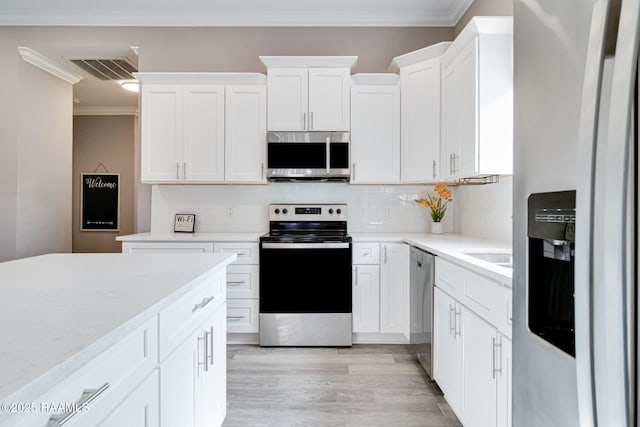 202 Saint Matthias Dr, Carencro, LA 70520 - kitchen featuring stainless steel appliances, ornamental molding, white cabinets, light wood-style flooring, and decorative backsplash