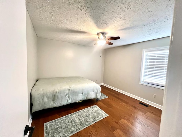 bedroom with visible vents, baseboards, a ceiling fan, wood finished floors, and a textured ceiling