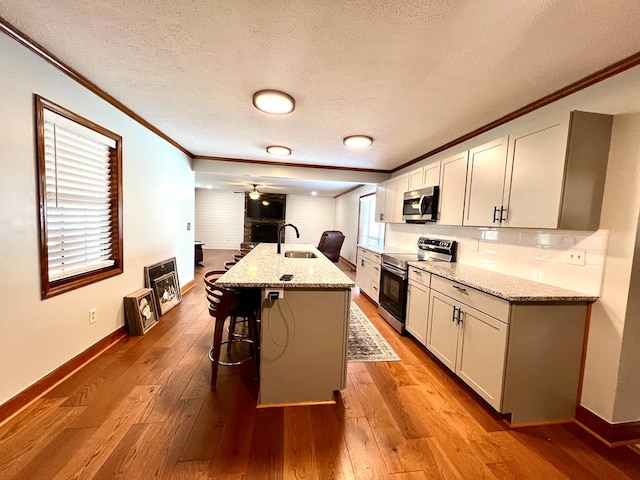 kitchen with stainless steel appliances, ornamental molding, a sink, and hardwood / wood-style floors