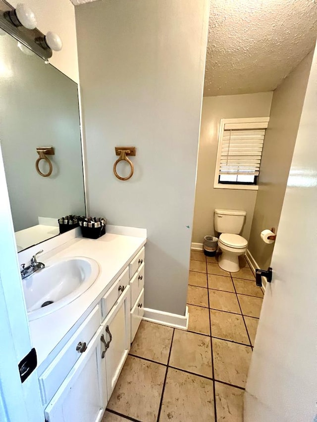 half bathroom featuring a textured ceiling, toilet, vanity, baseboards, and tile patterned floors