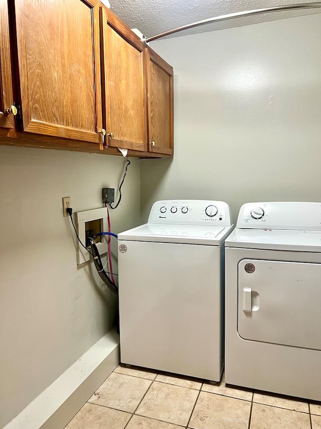 laundry area featuring light tile patterned floors, a textured ceiling, washing machine and dryer, and cabinet space