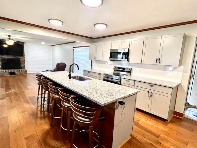 kitchen with ornamental molding, appliances with stainless steel finishes, light wood-type flooring, and a sink