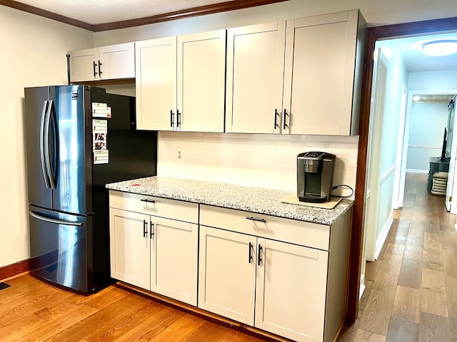 kitchen with light stone counters, light wood-style floors, ornamental molding, backsplash, and freestanding refrigerator