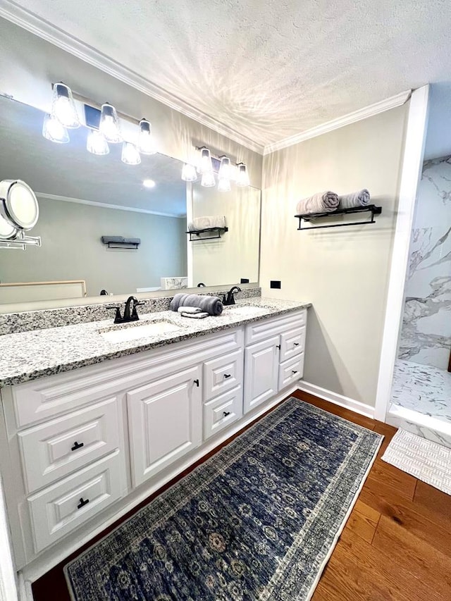 full bath featuring double vanity, ornamental molding, a sink, a textured ceiling, and wood finished floors