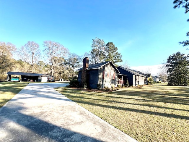 view of home's exterior with a carport, a chimney, concrete driveway, and a yard