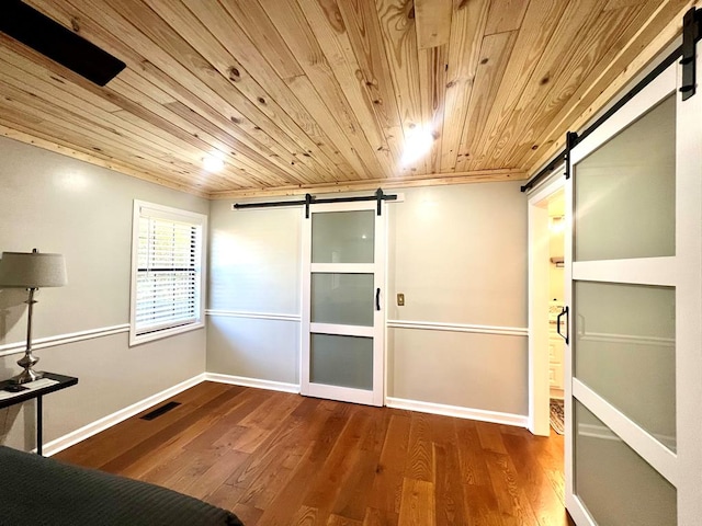 unfurnished bedroom featuring a barn door, wooden ceiling, wood finished floors, visible vents, and baseboards