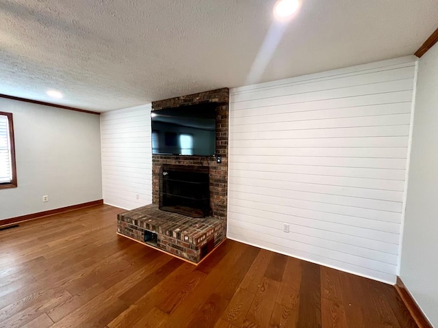 unfurnished living room featuring a textured ceiling, a fireplace, baseboards, and wood finished floors