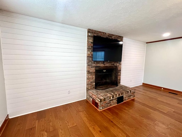 unfurnished living room featuring visible vents, a brick fireplace, a textured ceiling, wood finished floors, and baseboards