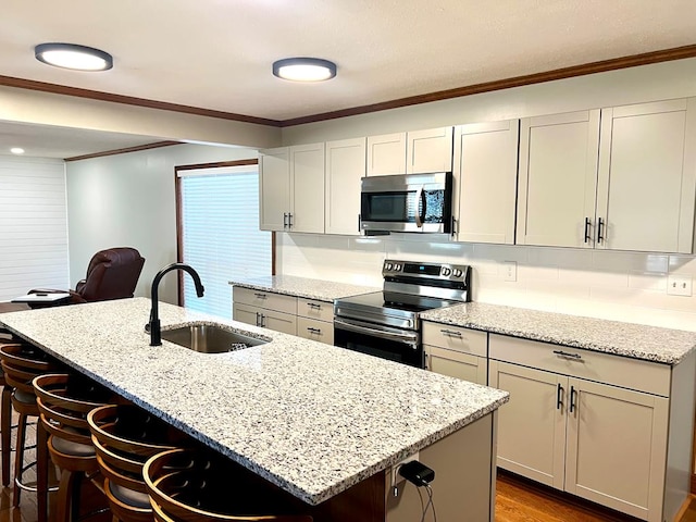 kitchen with light stone counters, ornamental molding, stainless steel appliances, a kitchen bar, and a sink