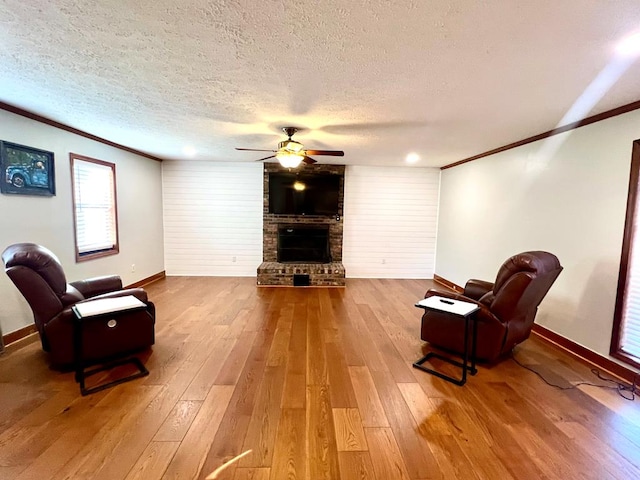 living area with a brick fireplace, wood-type flooring, a textured ceiling, and crown molding