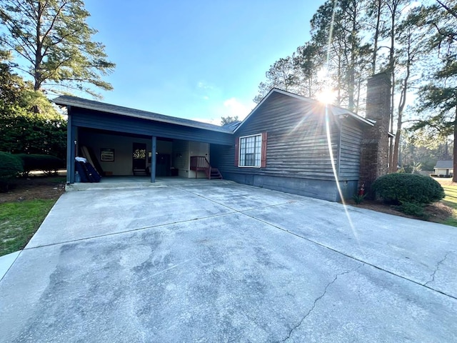 view of side of home with driveway, a carport, and a chimney