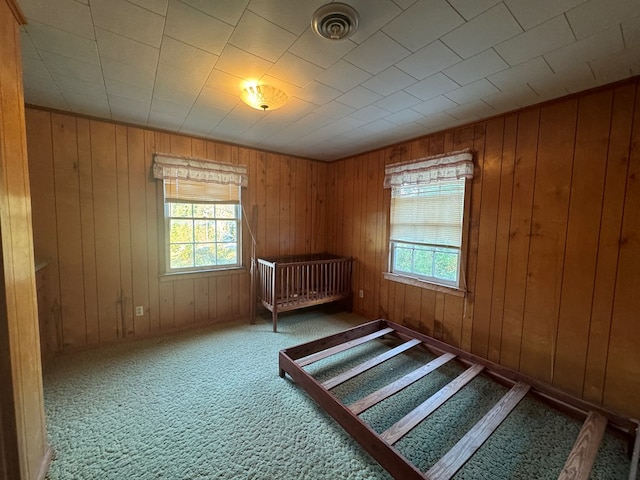 unfurnished bedroom with carpet flooring, wooden walls, and multiple windows