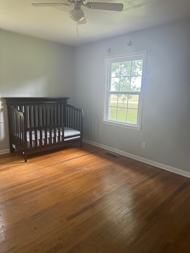 unfurnished bedroom featuring ceiling fan, wood-type flooring, and a nursery area