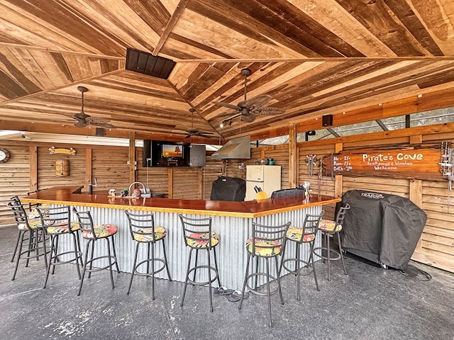 kitchen with lofted ceiling, a breakfast bar area, ceiling fan, and wood walls