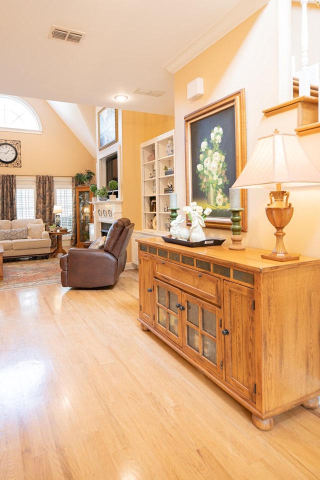 living room featuring vaulted ceiling, a fireplace, visible vents, and light wood-style floors