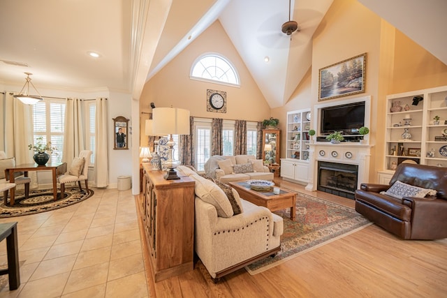 living room featuring a fireplace, light wood finished floors, visible vents, a ceiling fan, and high vaulted ceiling