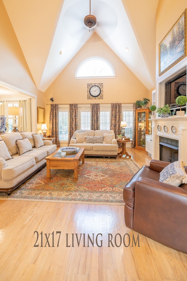 living area with high vaulted ceiling, plenty of natural light, a fireplace, and wood finished floors