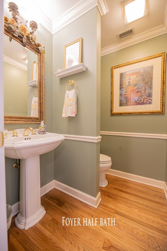 bathroom with baseboards, visible vents, wood finished floors, and ornamental molding