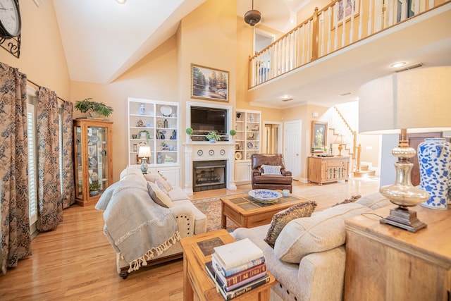 living room featuring visible vents, stairs, light wood-type flooring, a fireplace, and high vaulted ceiling