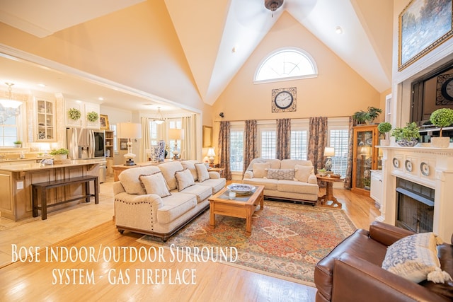 living area with high vaulted ceiling, a chandelier, a fireplace, and light wood-style flooring