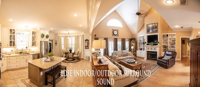 living room with a fireplace, visible vents, ornamental molding, ceiling fan, and high vaulted ceiling